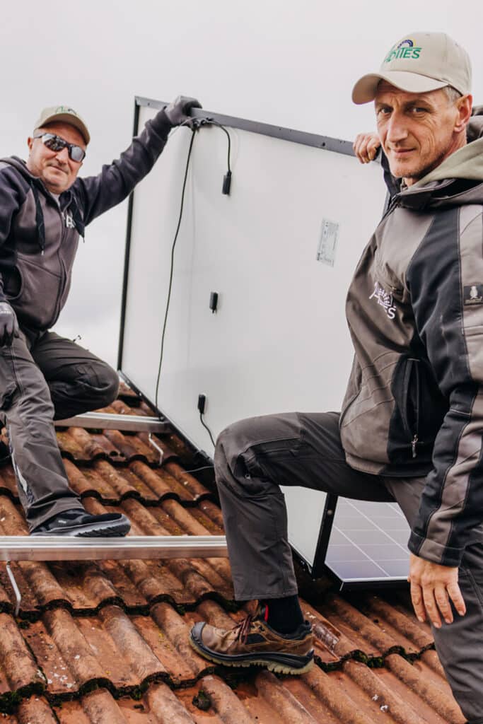 Zwei Männer installieren Solarpanel auf Dach.
